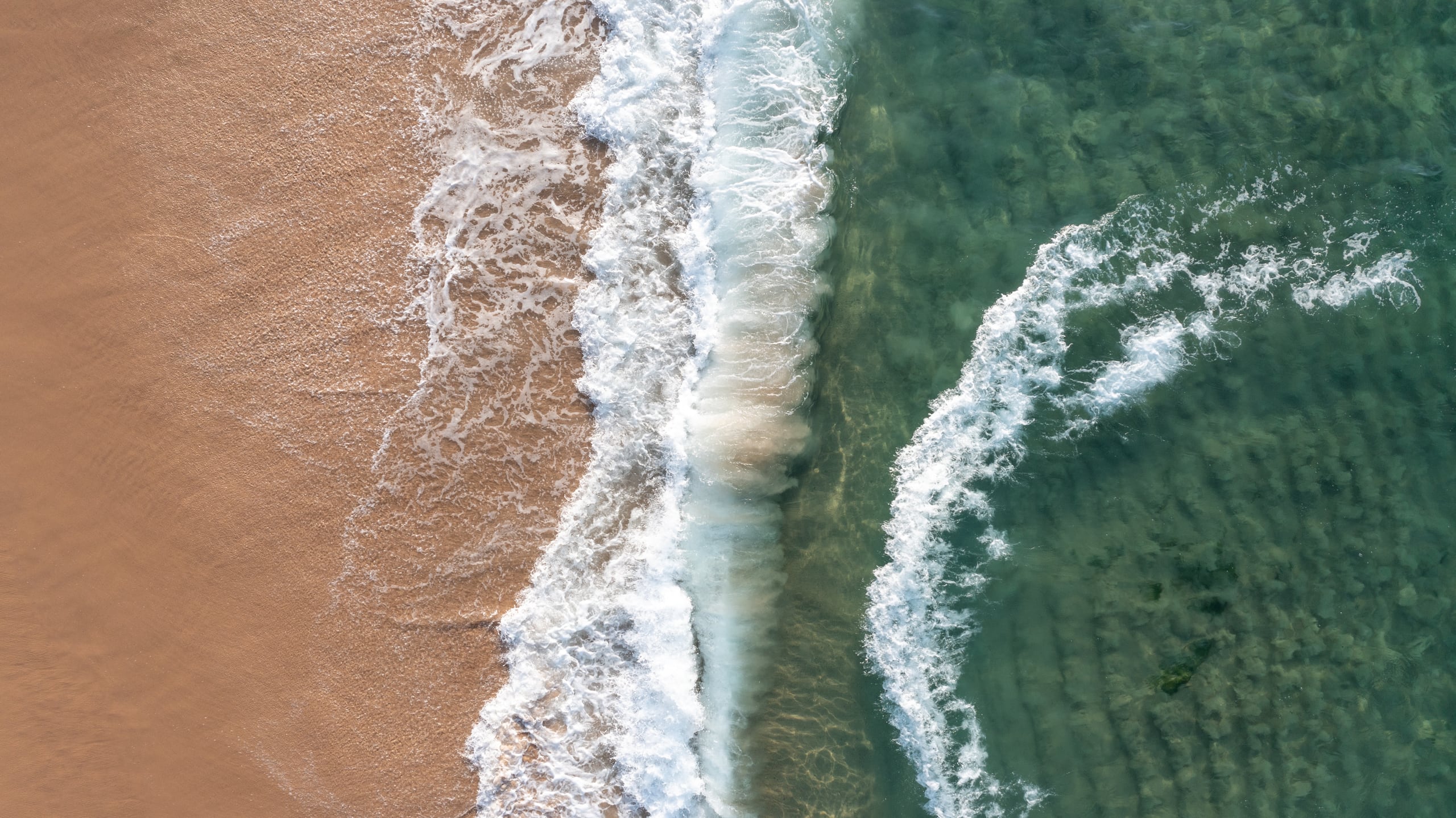 Aerial view of sand, surf and green sea at Praia do Farol da Barra in Salvador